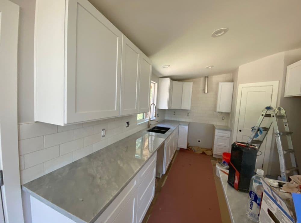Modern kitchen interior featuring white cabinets and a marble countertop. Renovation in progress.