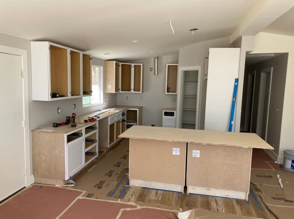 Open-concept kitchen under renovation with empty cabinets and an unfinished island.