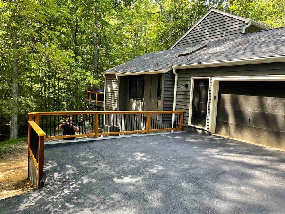 Modern home exterior with a wooden deck and garage, surrounded by lush greenery.