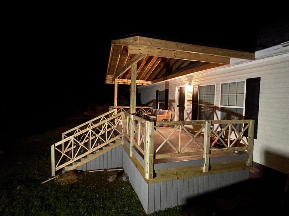 Nighttime view of a wooden deck with railing attached to a house, illuminated by outdoor lighting.