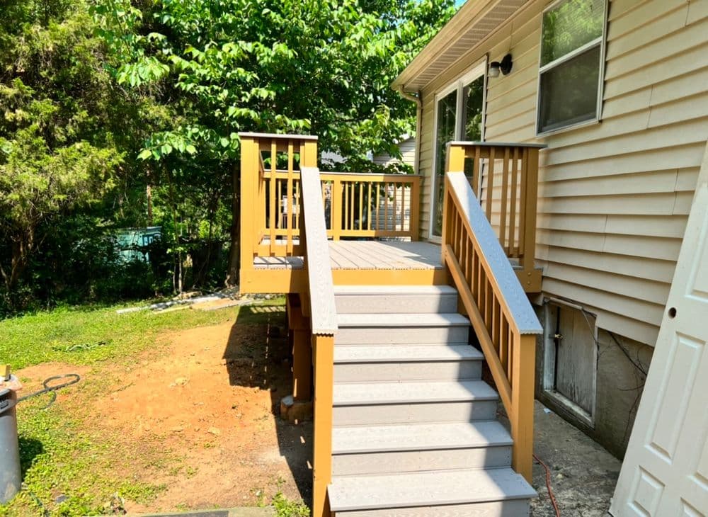 Accessible wooden deck with handrails leading to a house, surrounded by greenery.