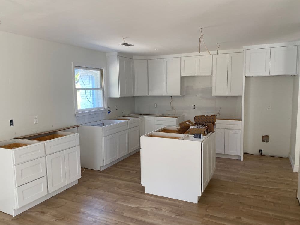 Modern kitchen renovation in progress with white cabinets and wood flooring.