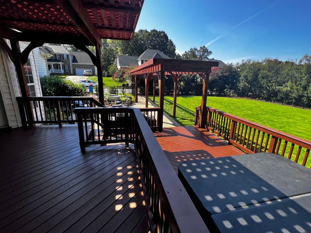 Spacious backyard deck with wooden railings, pergola, and lush green lawn.