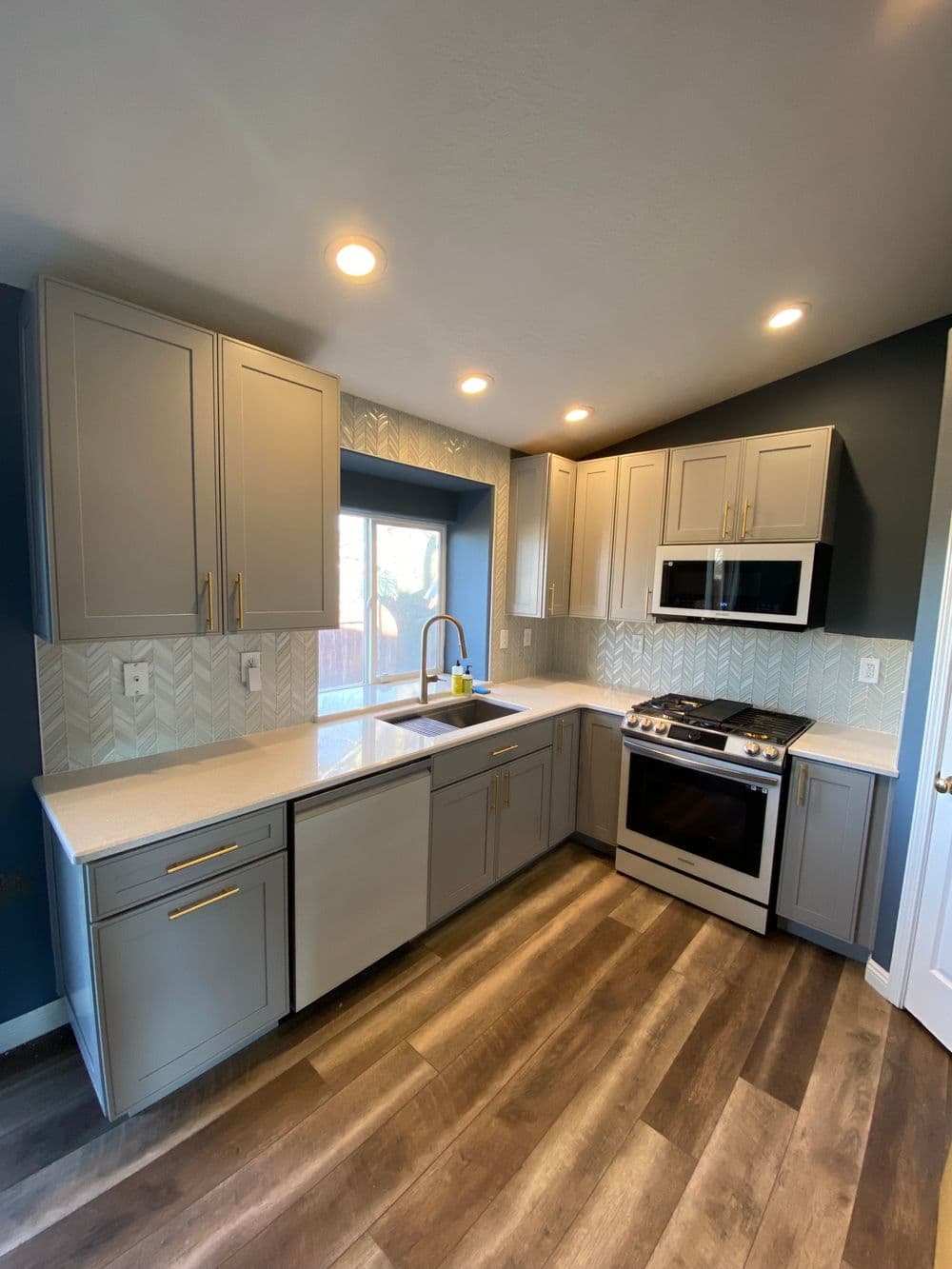 Modern kitchen with gray cabinets, stainless steel appliances, and herringbone backsplash.