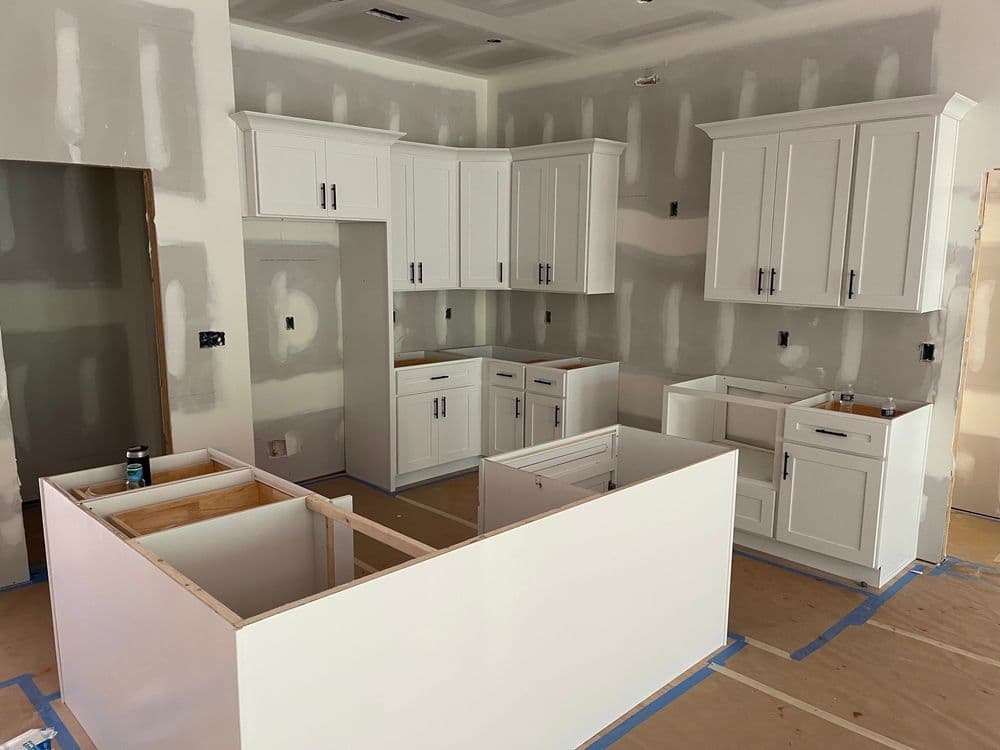 Modern kitchen with white cabinets and unfinished countertops, under construction.