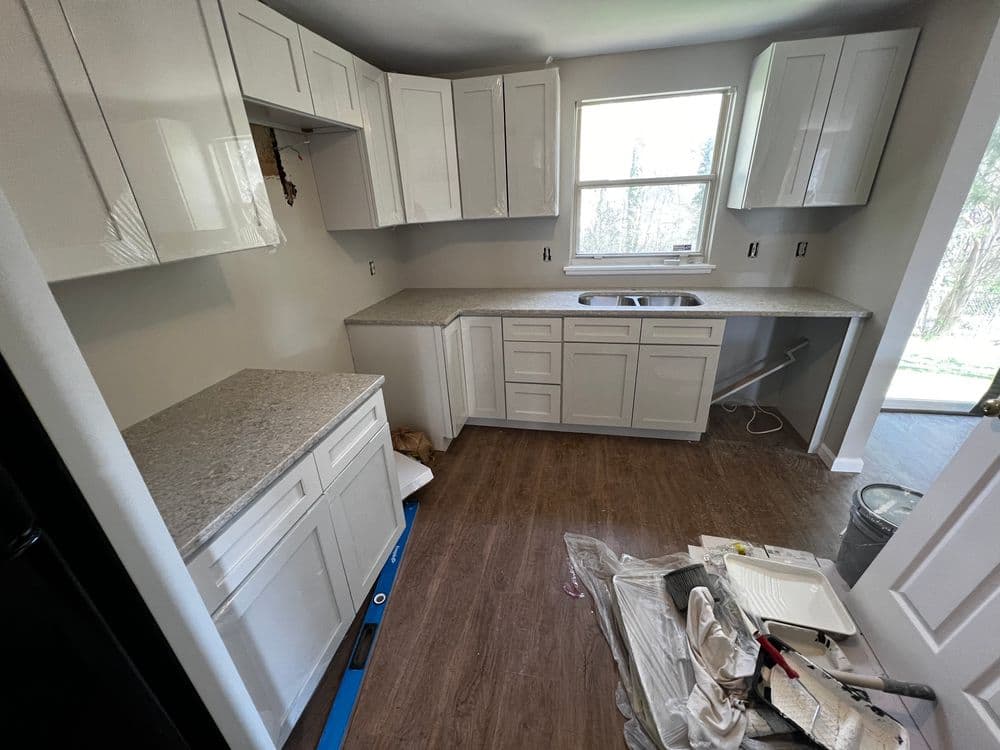 Modern kitchen with white cabinets, granite countertops, and unfinished flooring renovations.