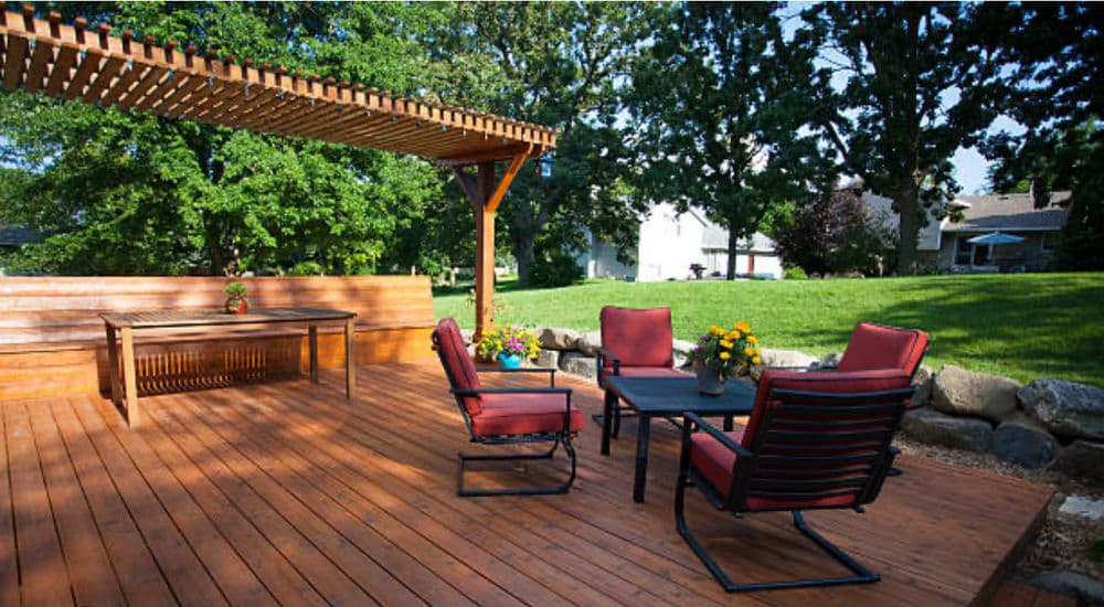 Cozy outdoor patio with seating, table, and vibrant flowers surrounded by greenery.