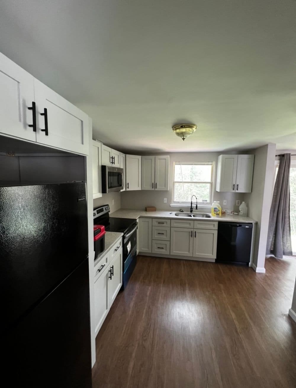 Modern kitchen with black appliances, light cabinetry, and spacious layout. Natural light from window.