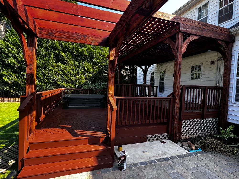 New wooden backyard deck with shaded pergola, surrounded by greenery and stone pathway.
