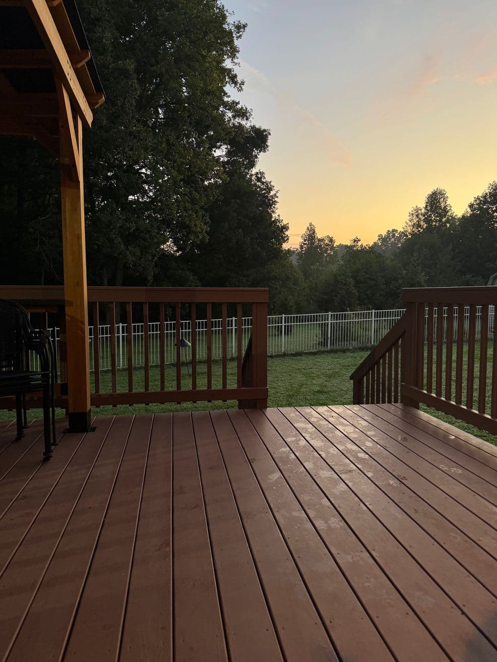 Sunset view from wooden deck overlooking green lawn and white fenced yard.