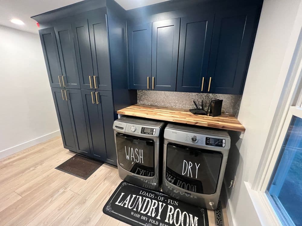 Modern laundry room with blue cabinets, wooden countertop, and stylish washer-dryer setup.