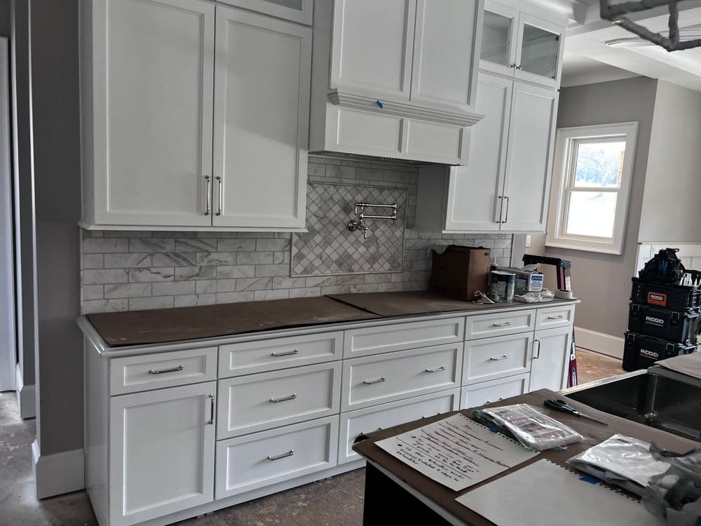 Modern kitchen with white cabinetry, gray backsplash, and unfinished countertops.