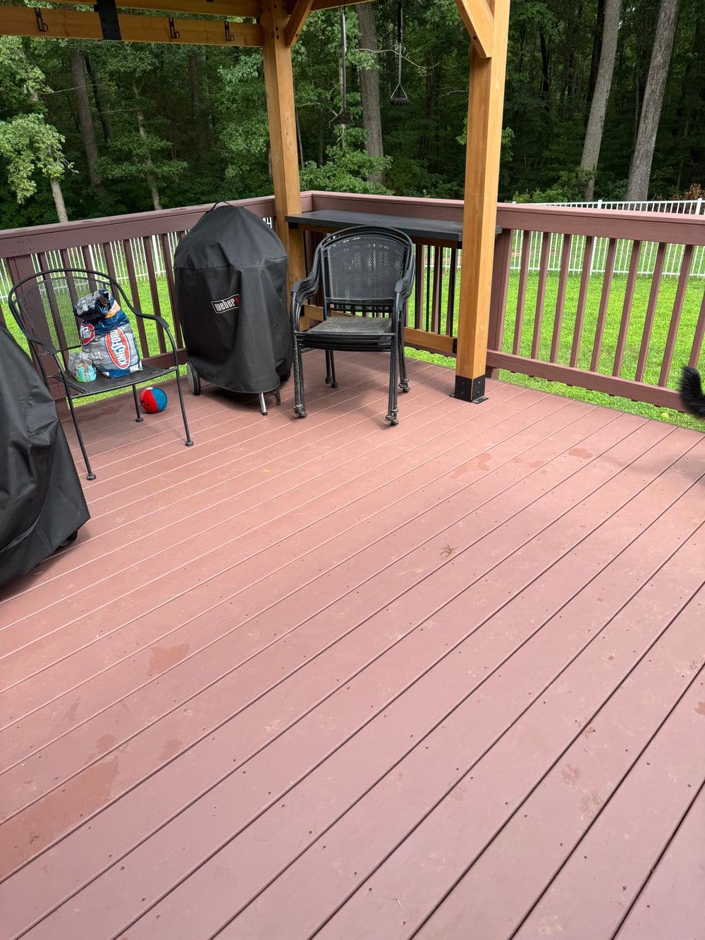 Deck area with furniture and grill covers surrounded by greenery and trees. Relaxing outdoor space.