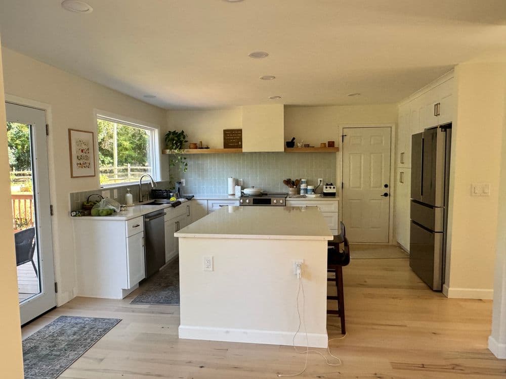 Modern kitchen with white cabinetry, island, and open layout, featuring natural light and wooden accents.