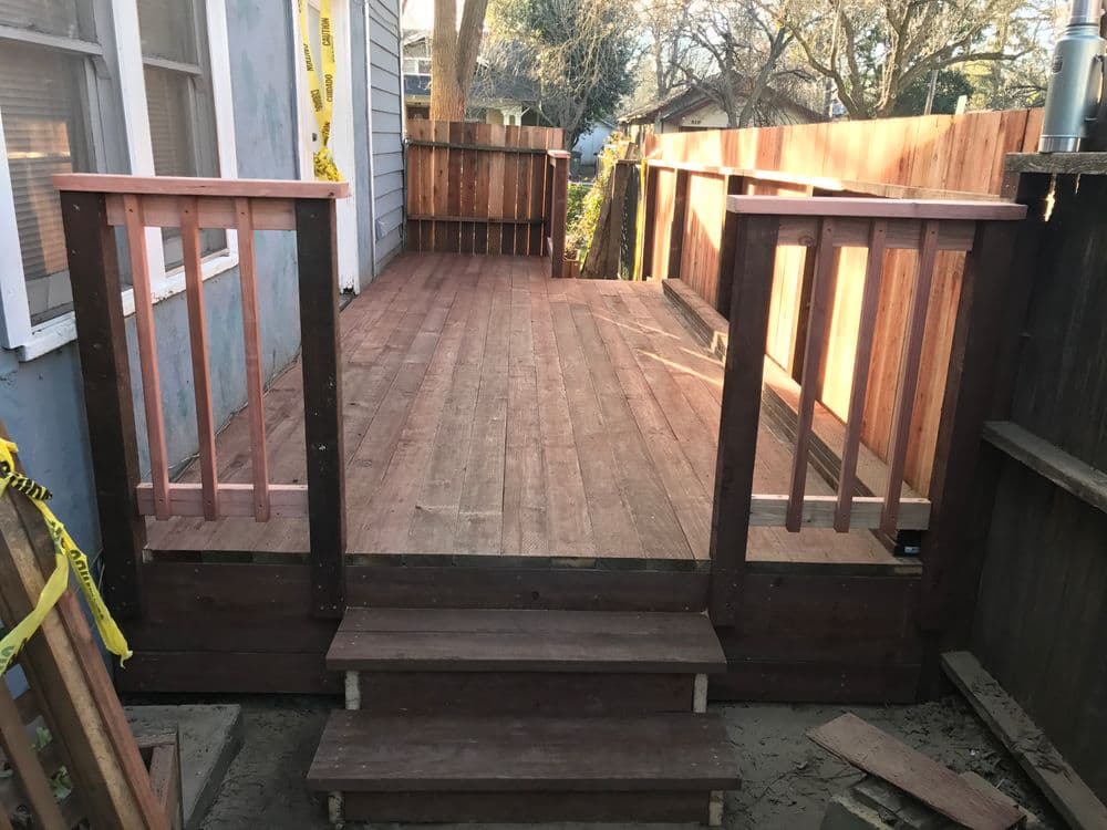 Newly constructed wooden deck featuring railing and steps, surrounded by yard greenery.