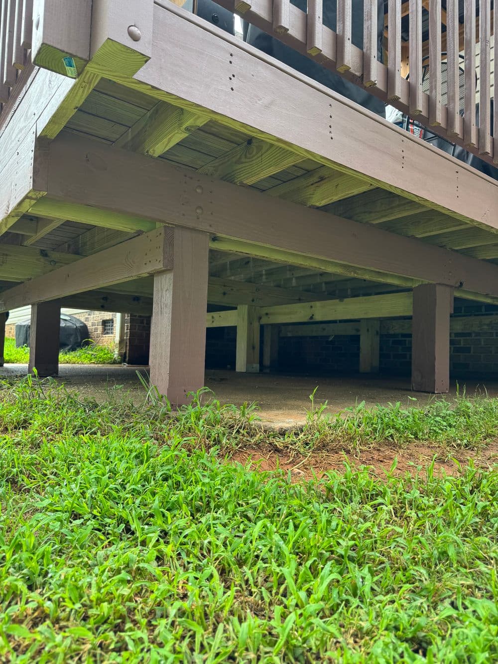 Underside of a wooden deck with support beams and grass underneath.