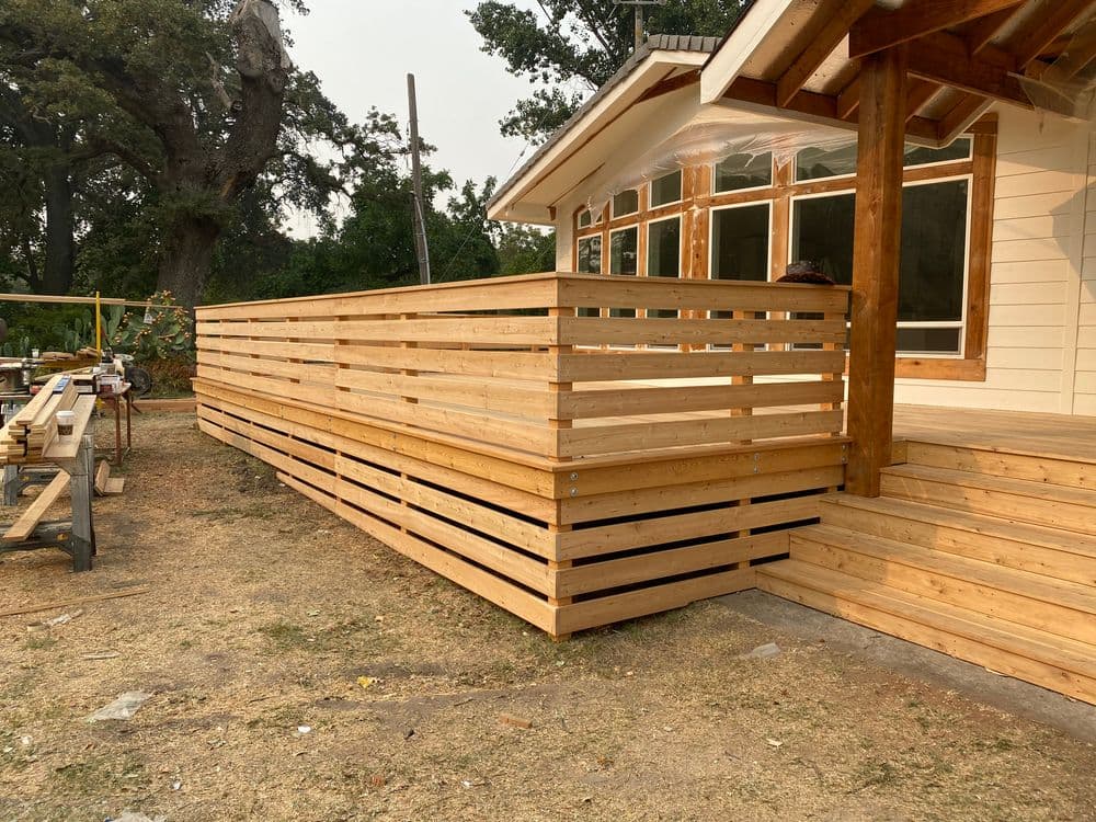 Modern wooden deck with horizontal slats extending from a home, surrounded by outdoor space.