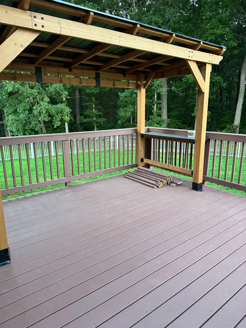 Wooden deck with a shaded pergola surrounded by green trees, offering a peaceful outdoor space.