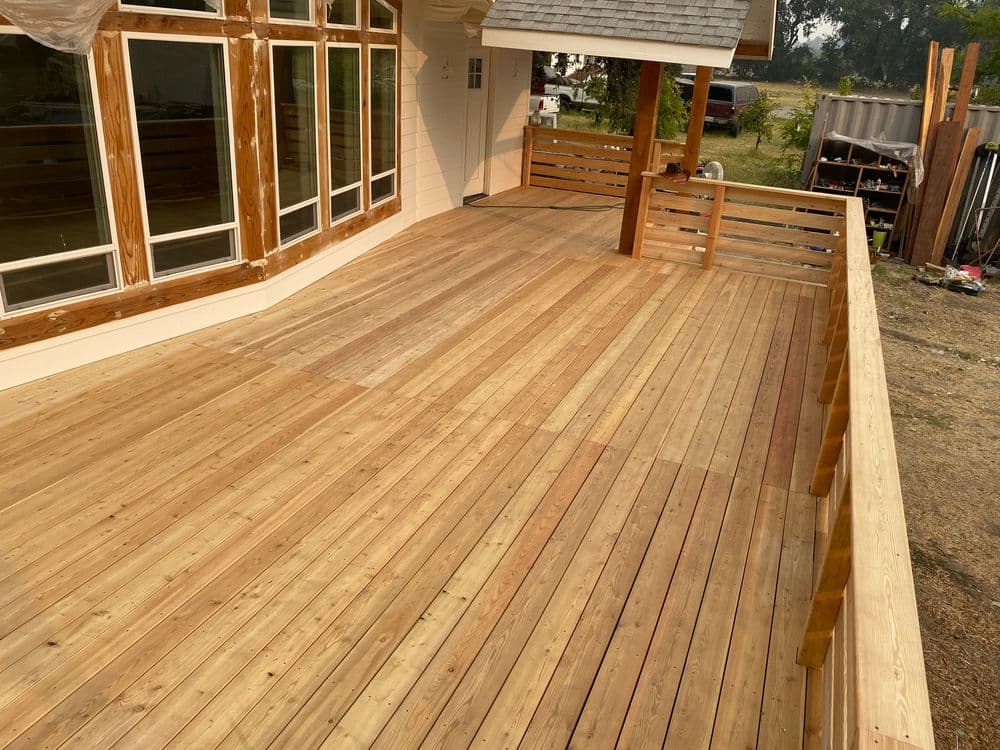 New wooden deck with polished boards and a railing, showcasing a spacious outdoor area.