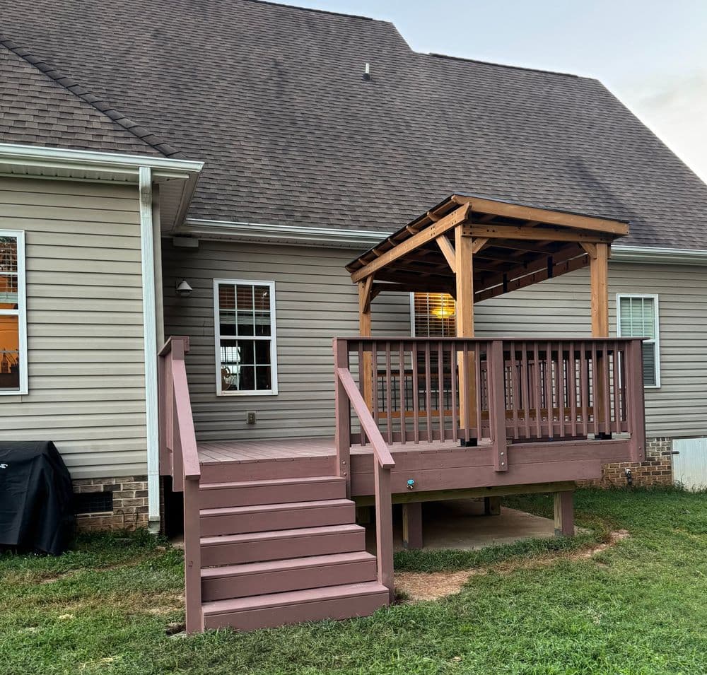 Modern wooden deck with steps leading to a house, surrounded by green lawn and siding.