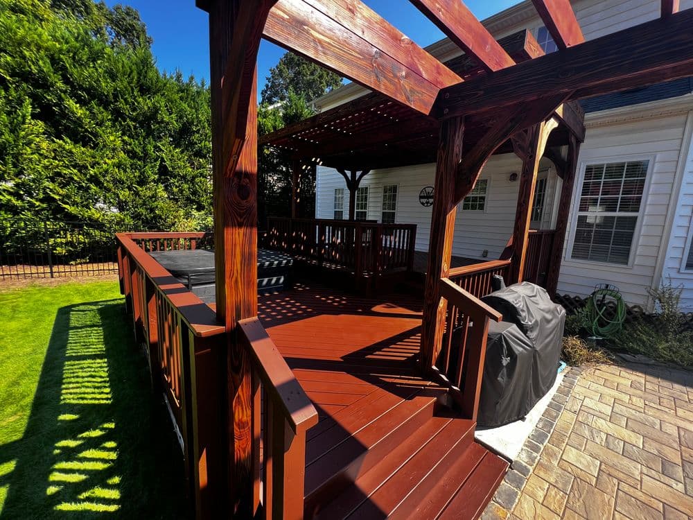 Modern wooden deck with pergola and patio furniture in a residential backyard setting.
