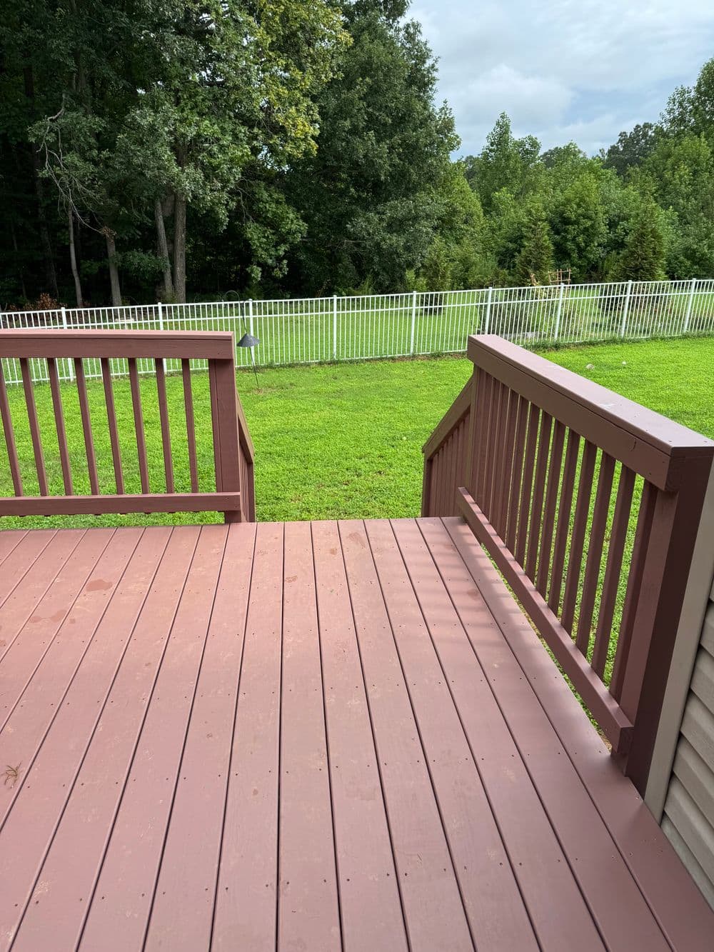 View from a wooden deck leading to a green lawn with a white wooden fence.