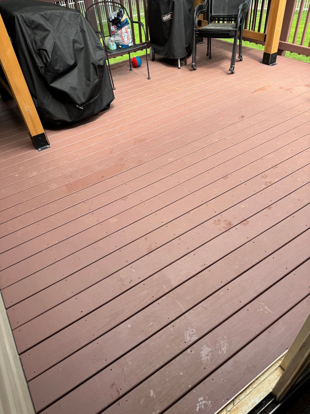 Clean wooden deck with outdoor furniture and a colorful ball on the grass.