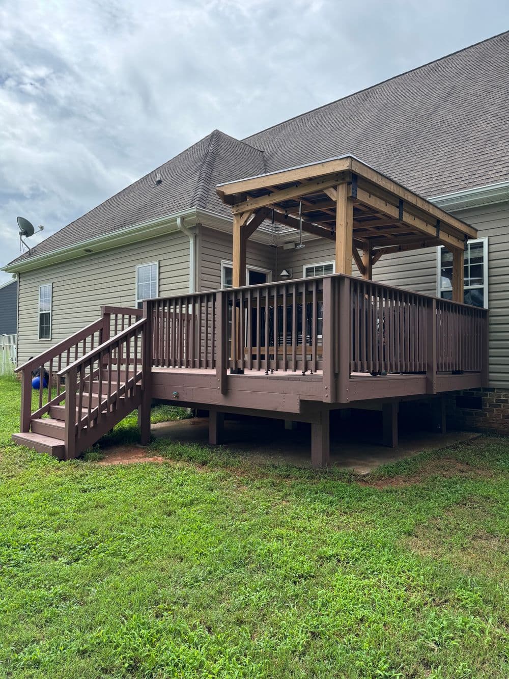Wooden deck with pergola and stairs, set against a house and grassy yard.