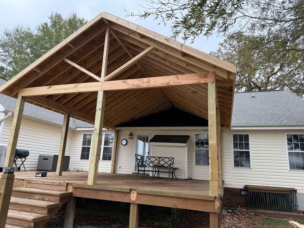 Newly constructed wooden porch with a gabled roof, wooden steps, and outdoor seating area.