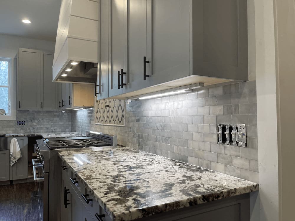 Modern kitchen with gray cabinetry, marble countertops, and elegant tile backsplash.