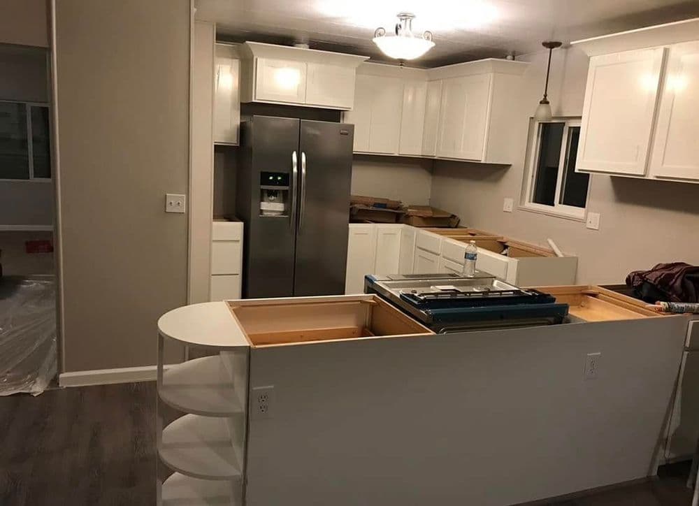 Modern kitchen renovation with white cabinetry, stainless steel fridge, and open layout.