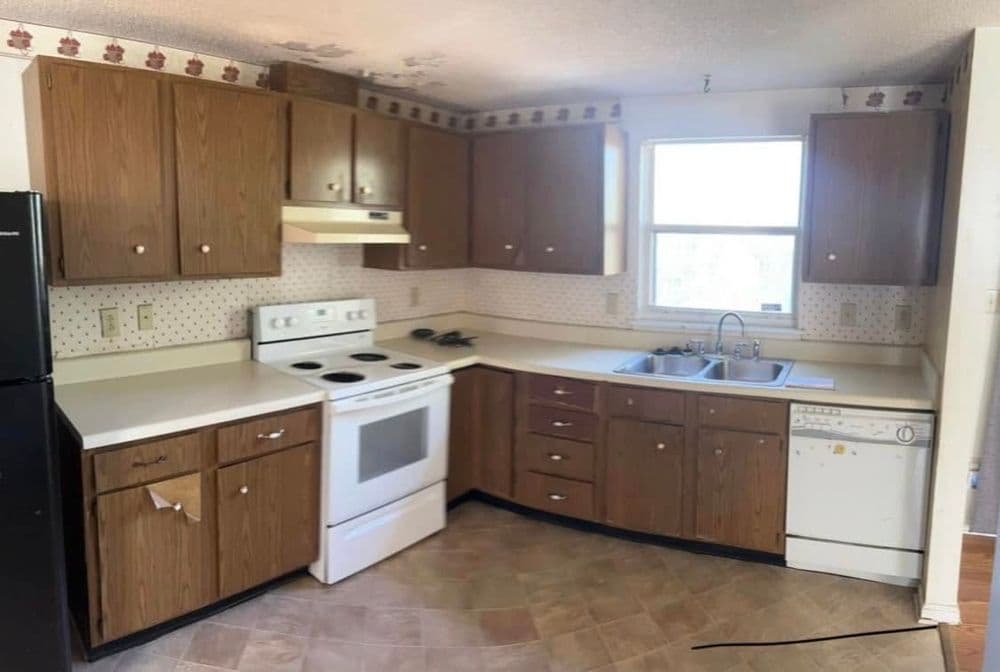 Compact kitchen with wooden cabinets, white appliances, and a window for natural light.