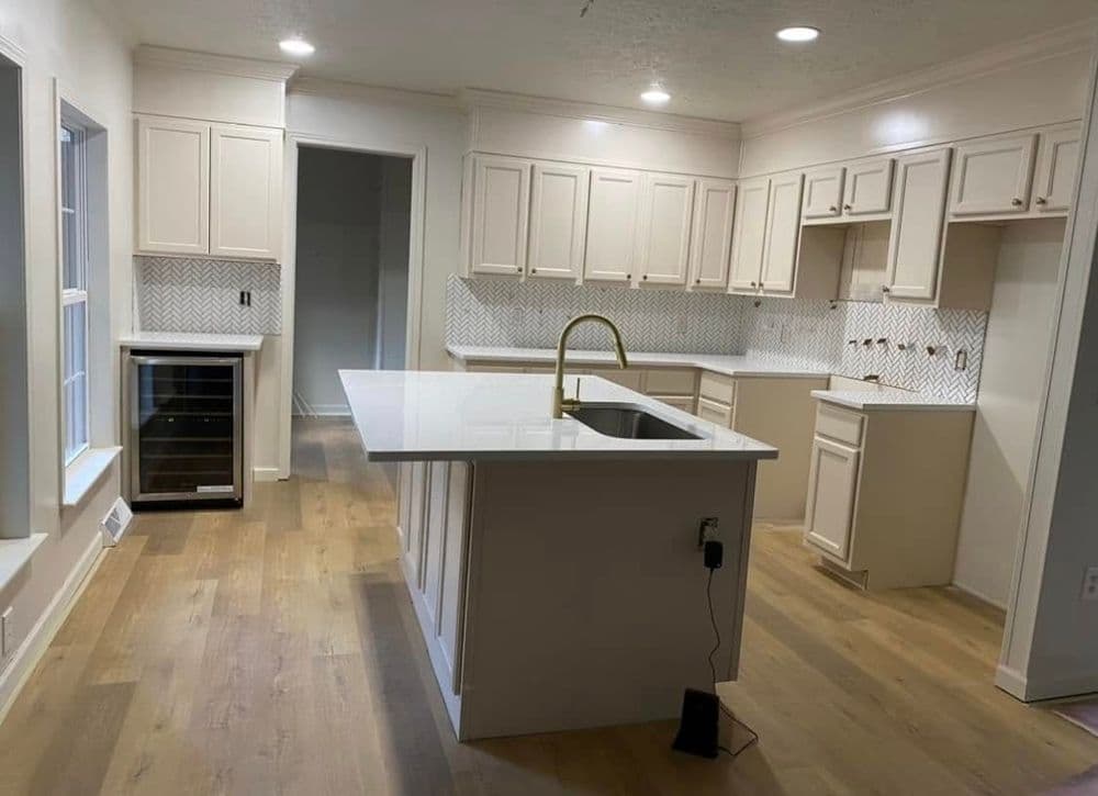 Modern kitchen with white cabinetry, large island, stainless steel sink, and wood flooring.