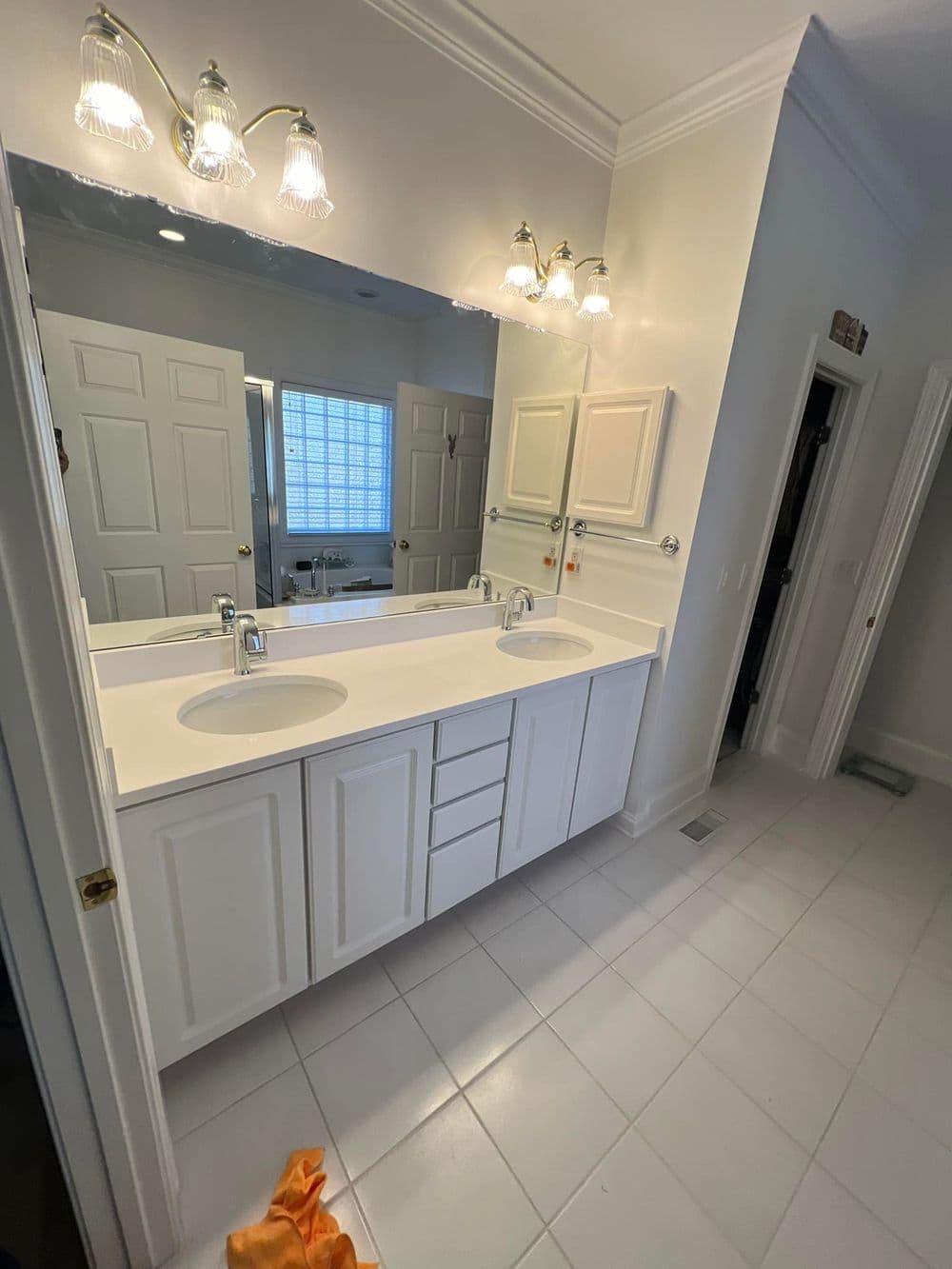 Spacious bathroom with dual sinks, vanity lighting, and white tile flooring.