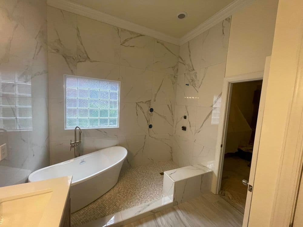 Modern bathroom featuring a freestanding tub, marble walls, and glass block window.