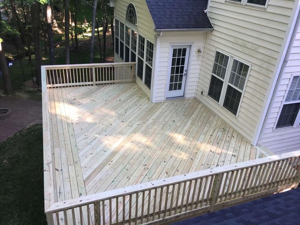 Spacious wooden deck with railing, surrounded by trees, attached to a home.