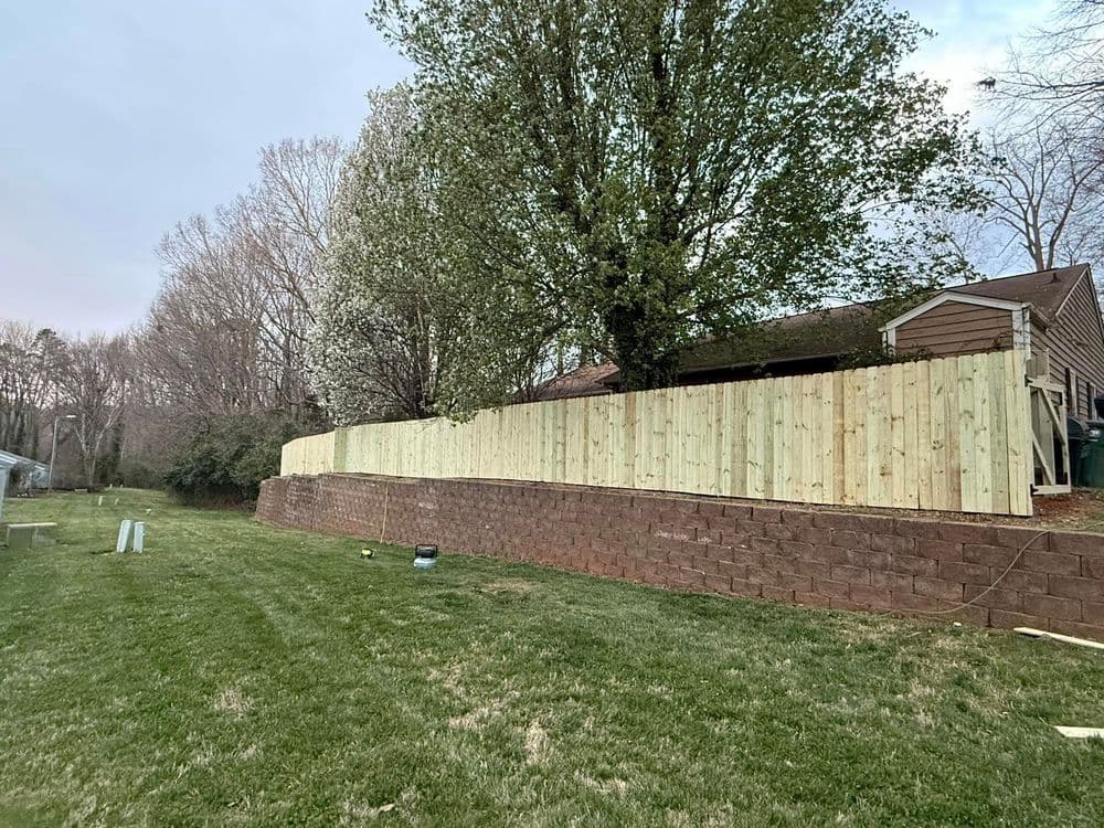 New wooden fence installed along backyard, surrounded by trees and grassy area.