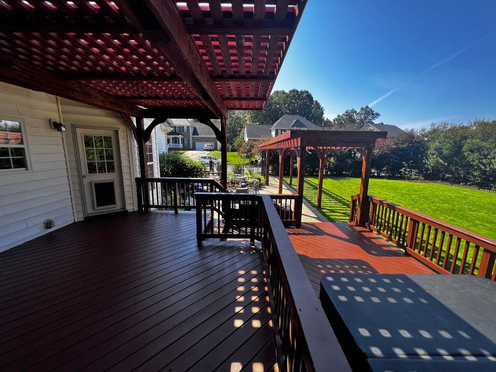 Spacious wooden deck with pergola overlooking a landscaped backyard on a sunny day.