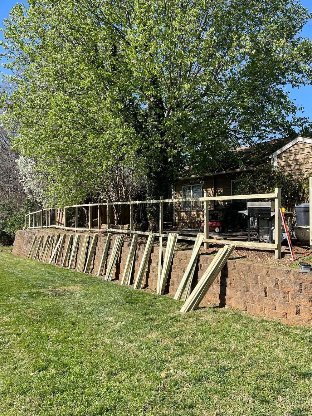 Construction of a wooden fence with stacked materials in a backyard setting.