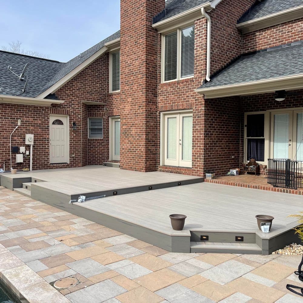 Modern outdoor deck built with composite materials next to a brick home, featuring landscaping.