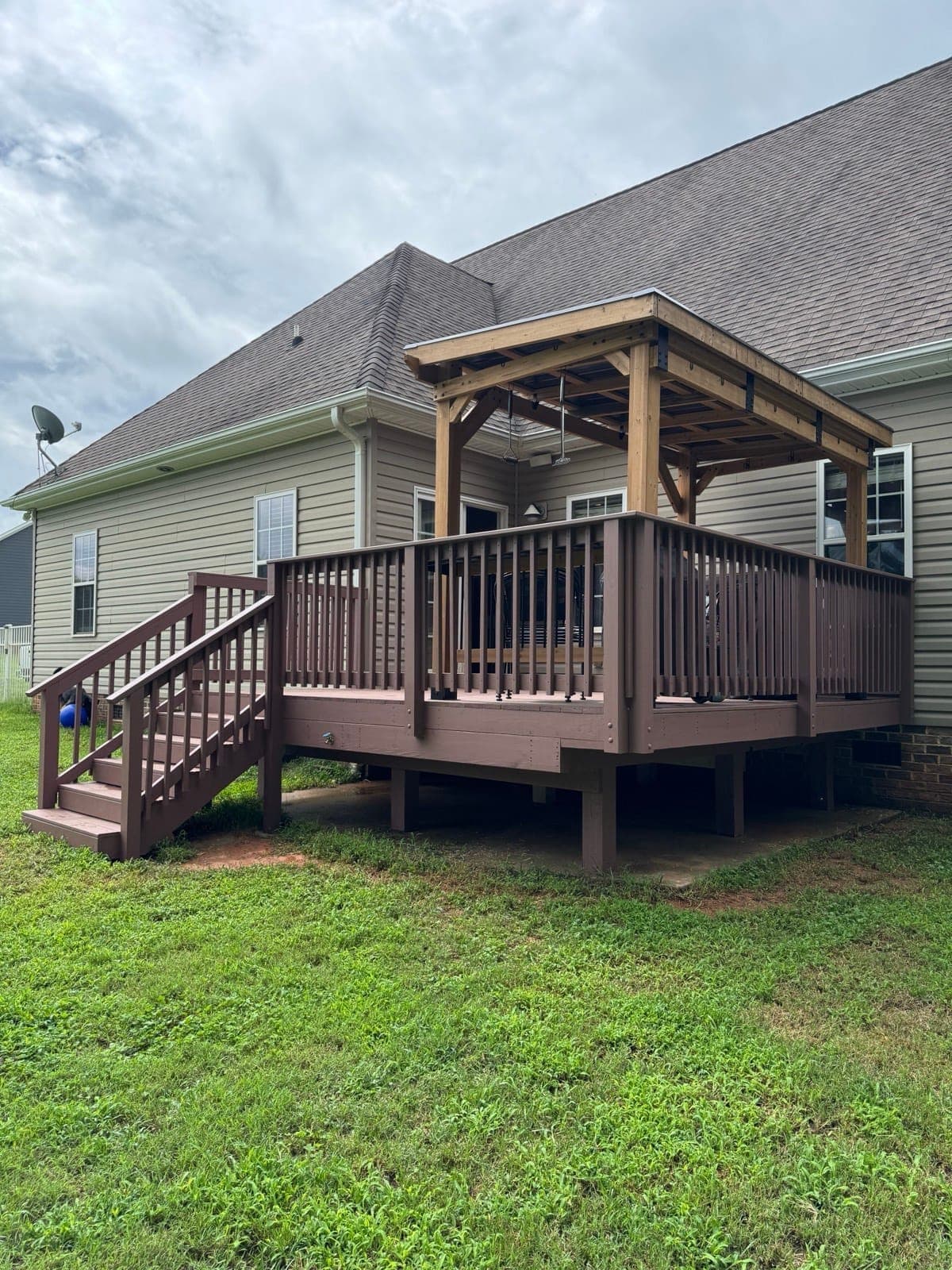 Raised brown-stained wood deck with a cedar pavilion over the grilling end, behind a tan-sided home in Mint Hill NC